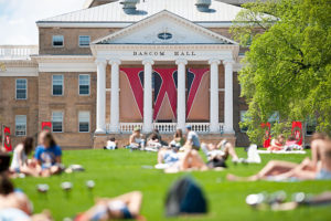UW-Madison students relaxing in the grass on Bascom Hill with Bascom Hall and green tree in the background.