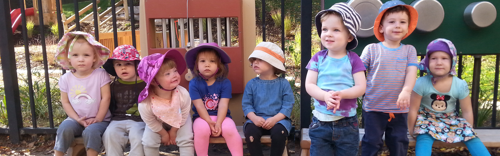 Six children wearing hats sitting on outdoor play equipment.