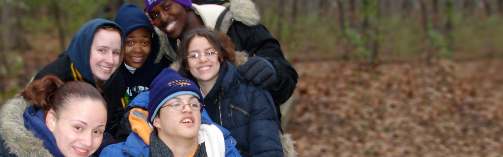 Group of 5 smiling adolescents in winter gear outside with leaves on the ground.