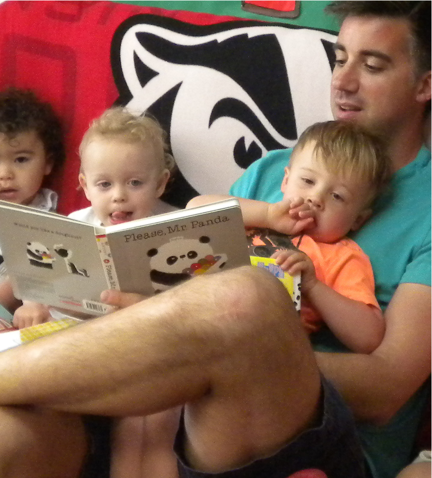 A man reads a book to three young children in his lap