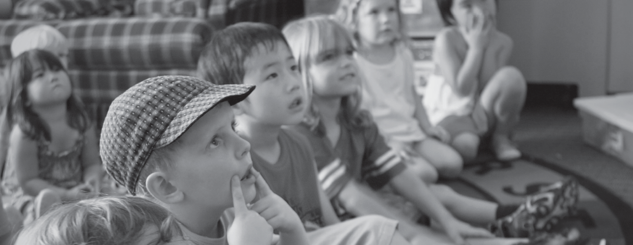 Seven preschoolers sitting on the floor looking up