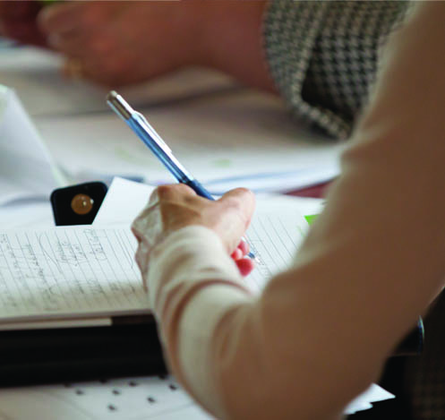 A person writing in a notebook with a pencil.