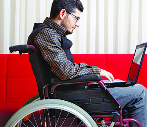 Young man in a wheelchair using a laptop.