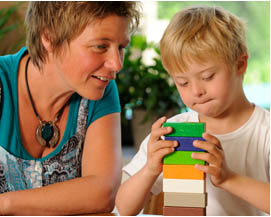 child building a stack of blocks with teacher watching