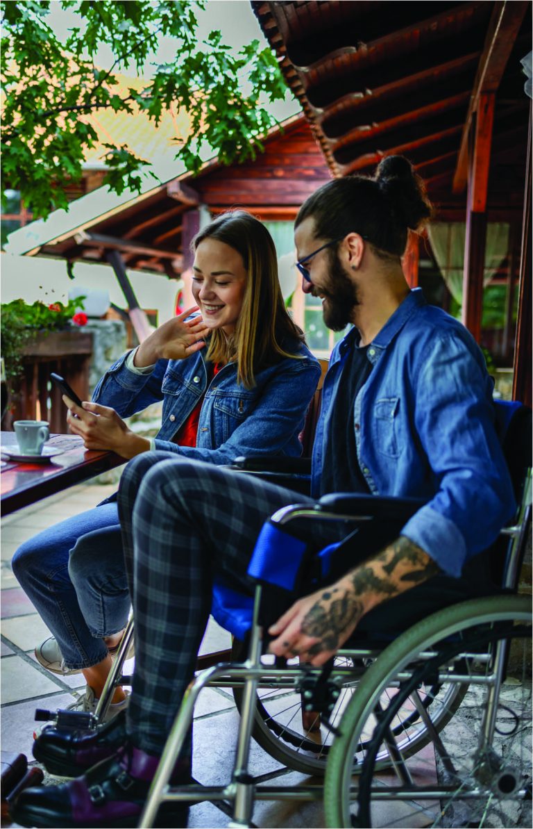 Man in wheelchair talking to woman who is showing him something on her phone